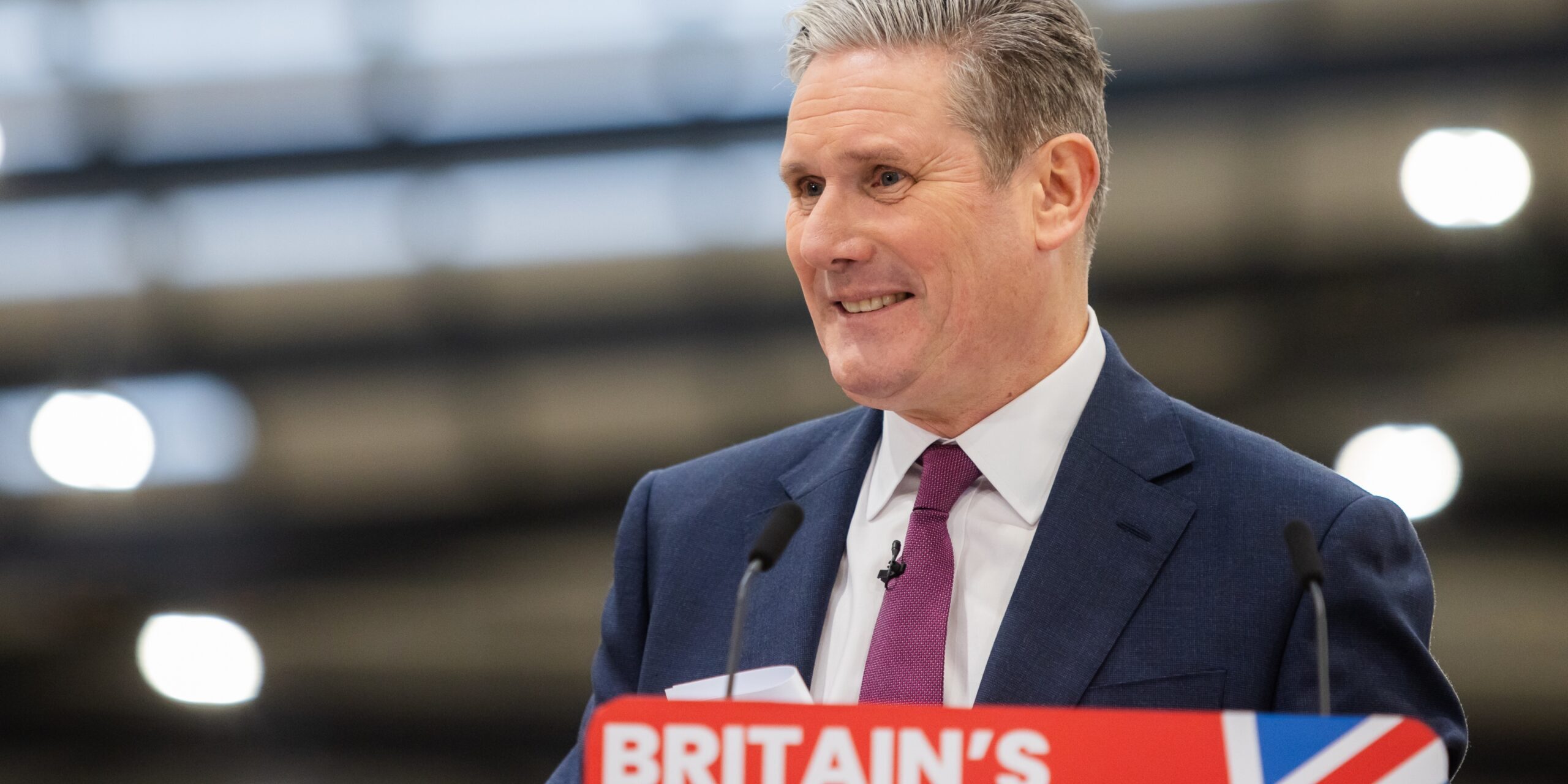 Keir Starmer smiling behind a podium that says 'Britain's Future' on it