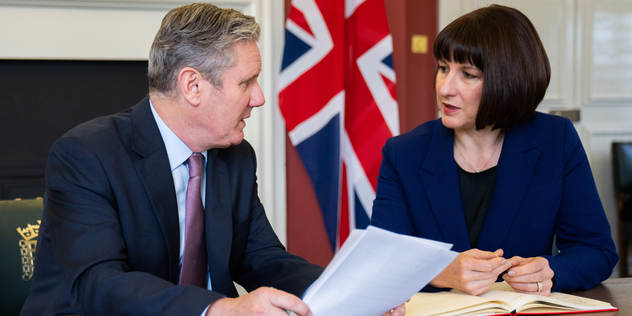 Keir Starmer and Rachel Reeves sat at a table, looking at each other in front of a Union flag