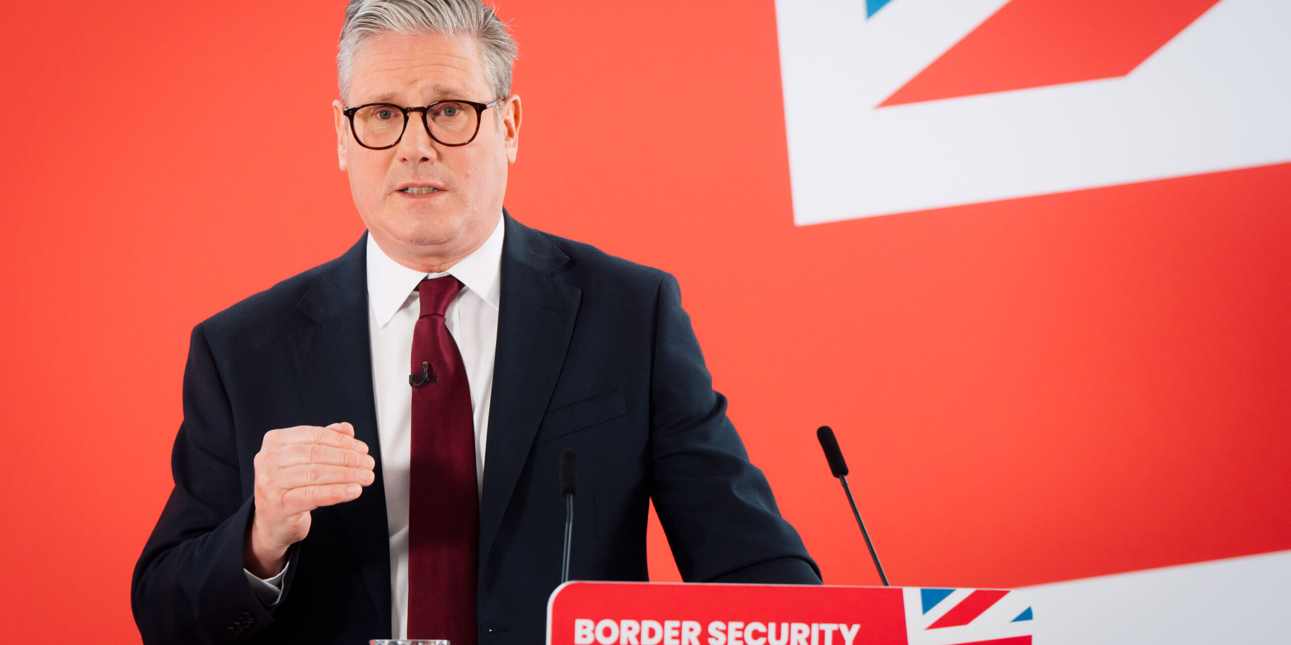 Keir Starmer standing at a podium in front of a Union Jack backdrop. The podium says 'Border security' on it