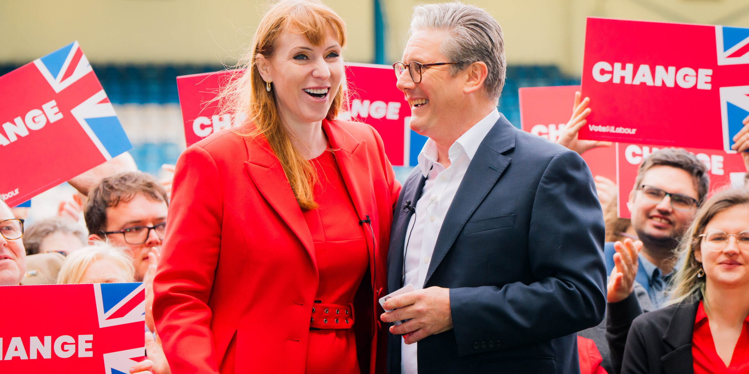Keir Starmer and Angela Rayner stand laughing in front of a crowd holding red placards that say 'Change' on them