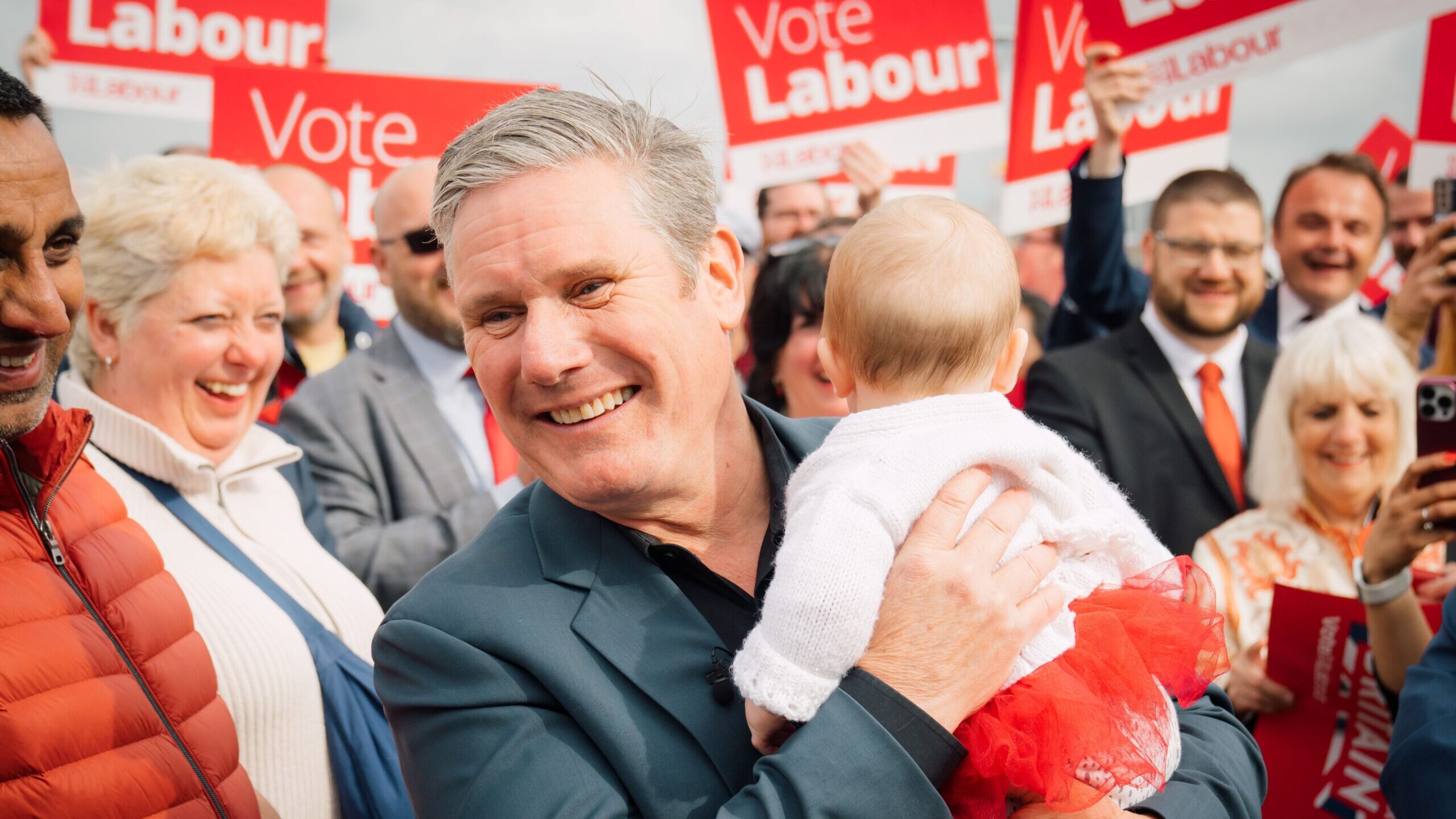 Keir Starmer holding a baby in front of placards reading Vote Labour