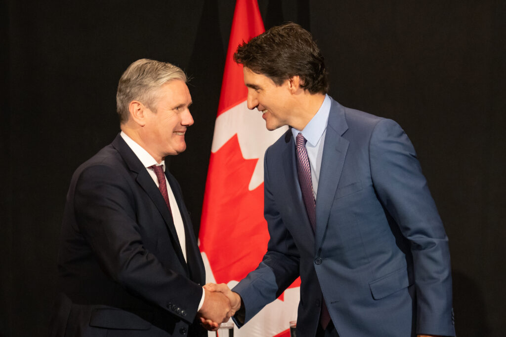 Keir Starmer shaking hands with Justin Trudeau, Prime Minister of Canada, in front of the Canadian flag.