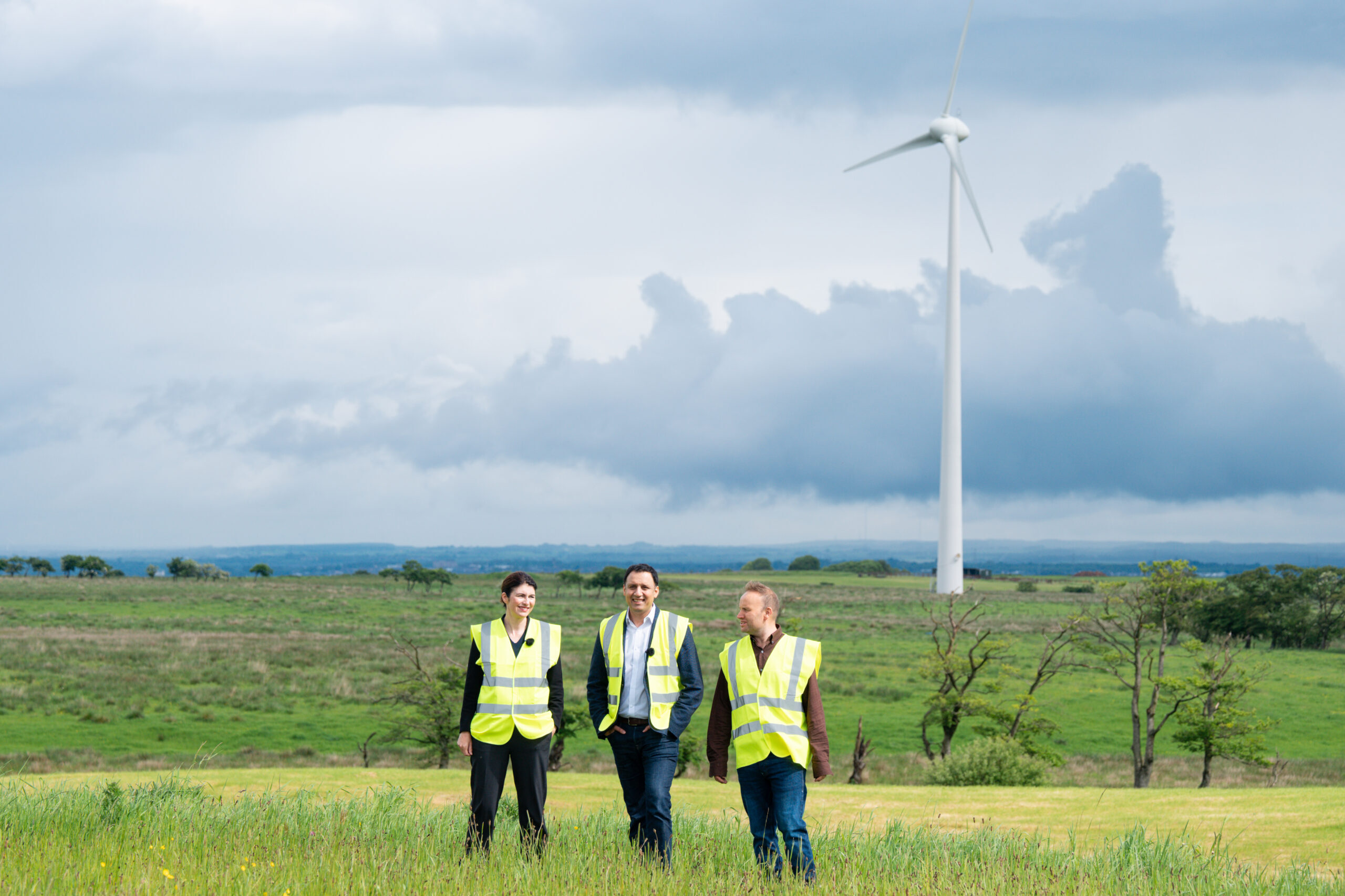 Anas Sarwar and two people standing in a field in front of a wind turbine