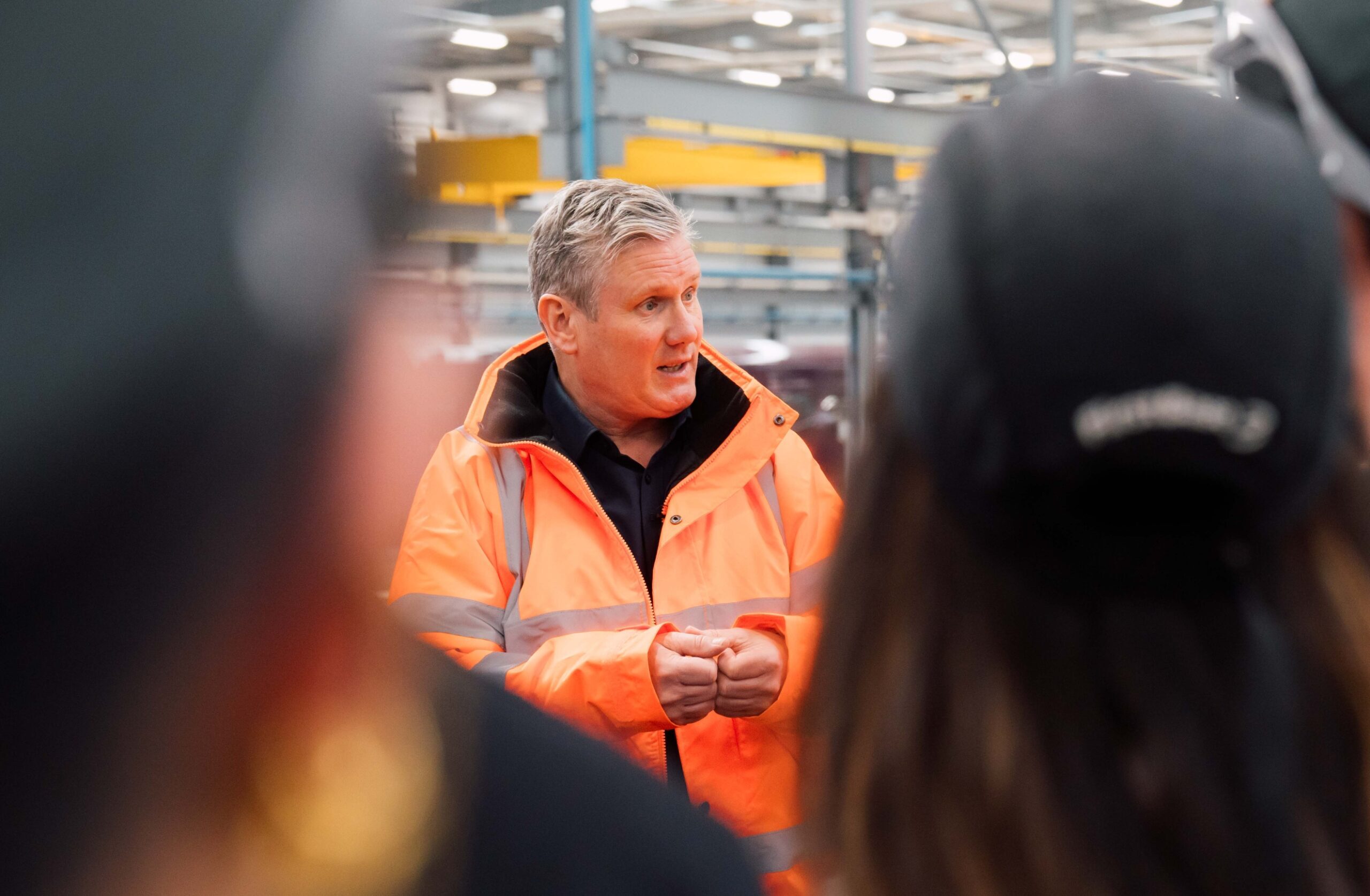 Keir Starmer speaking on a factory visit, wearing a high visibility orange coat.