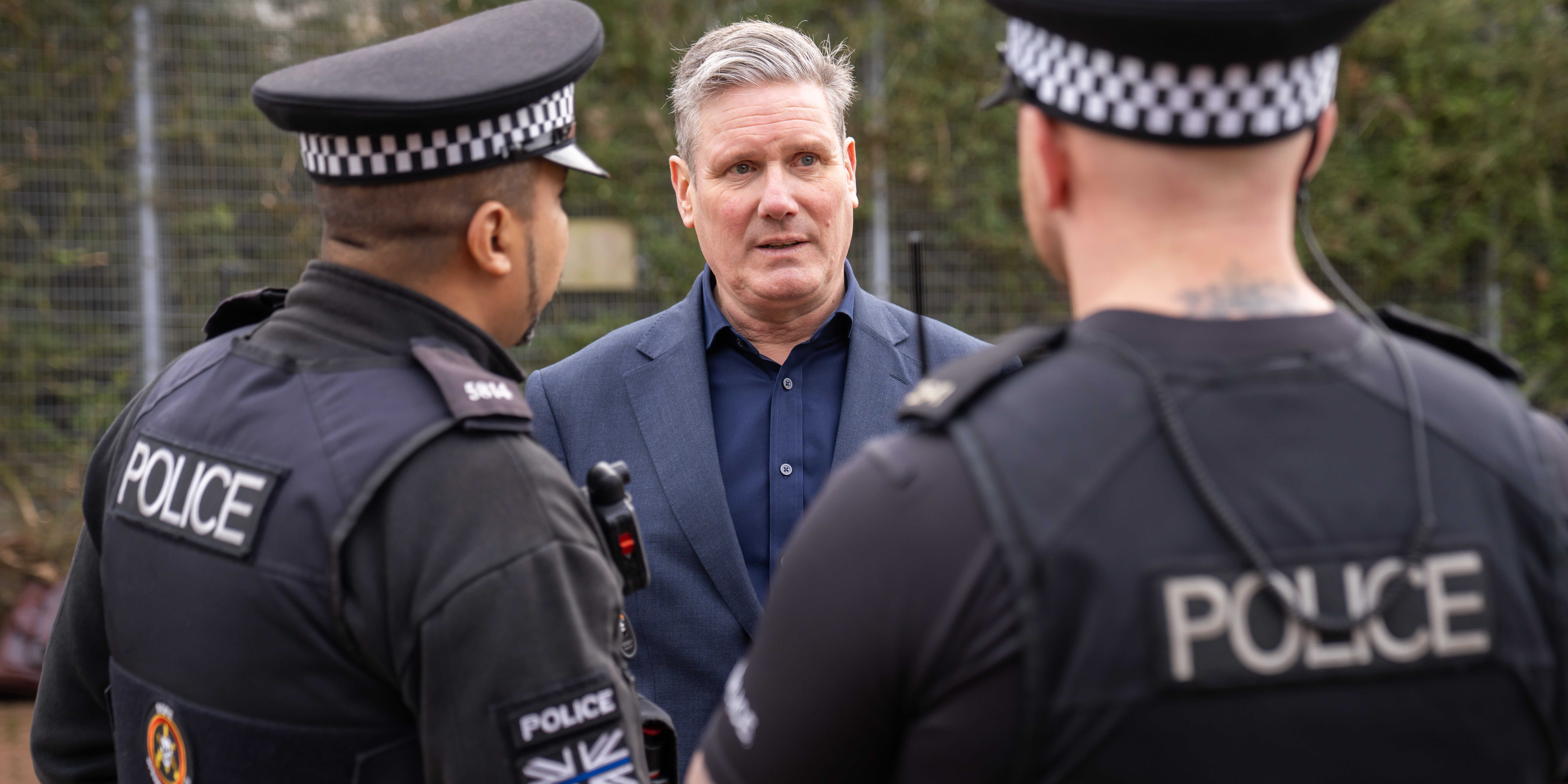 Photo of Keir Starmer facing the camera and speaking to two police officers with their backs to the camers