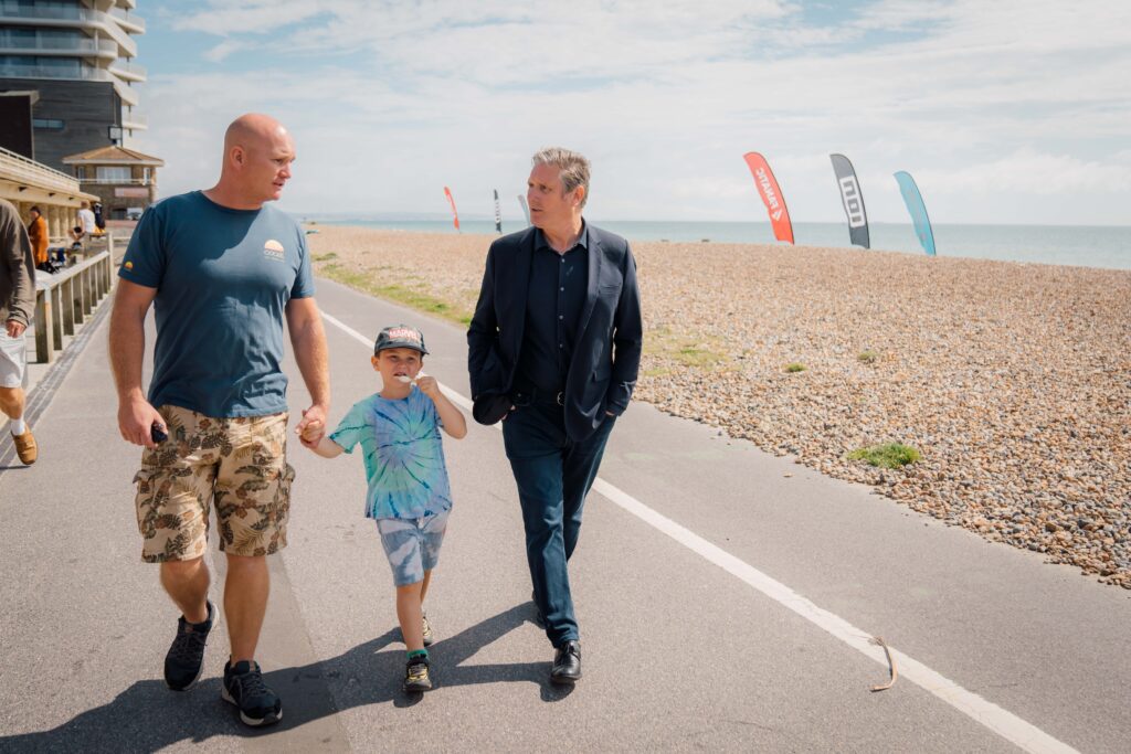 Keir Starmer talking and walking with a father and son beside the sea.