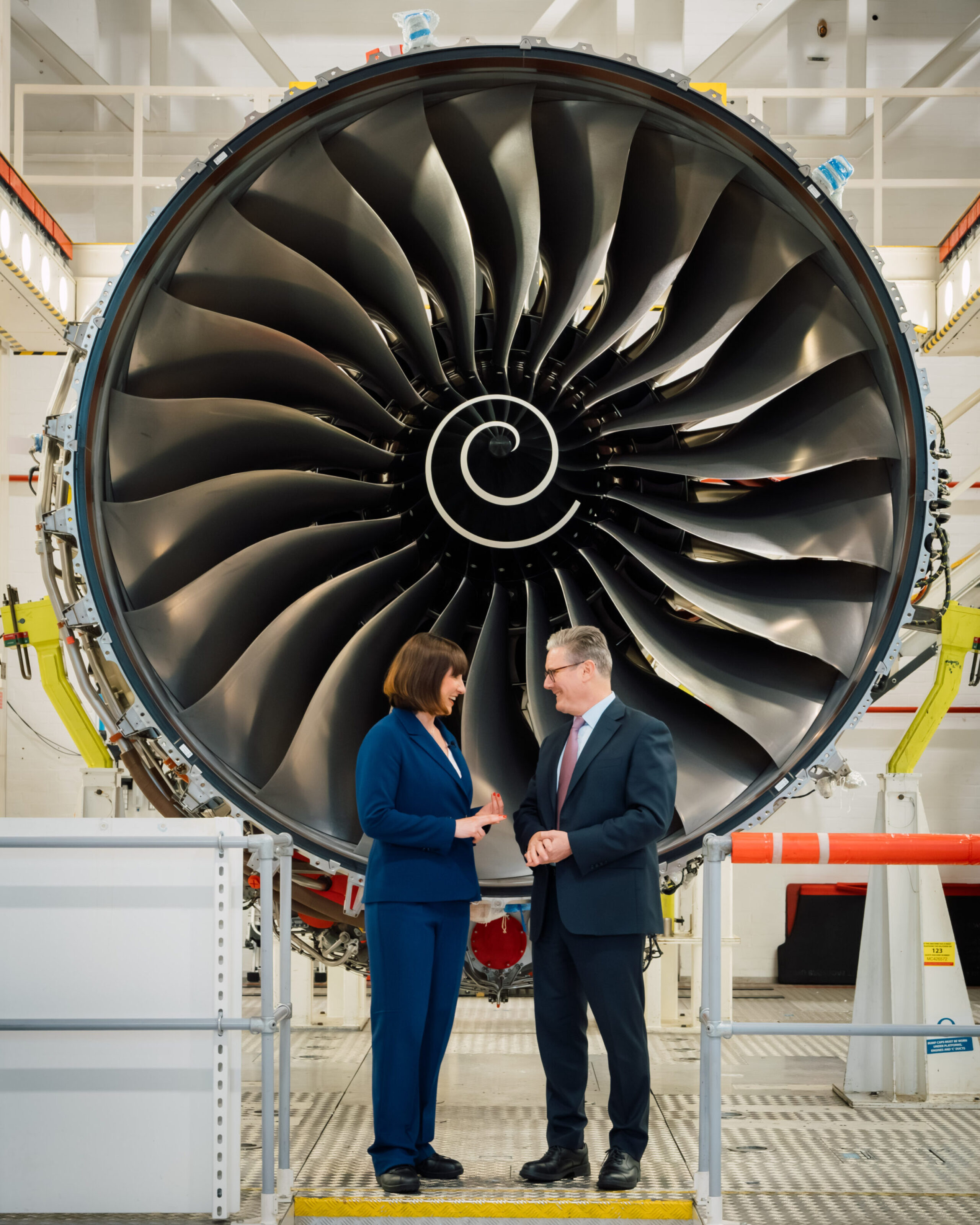Keir Starmer and Rachel Reeves standing side by side talking in front of an engine turbine.