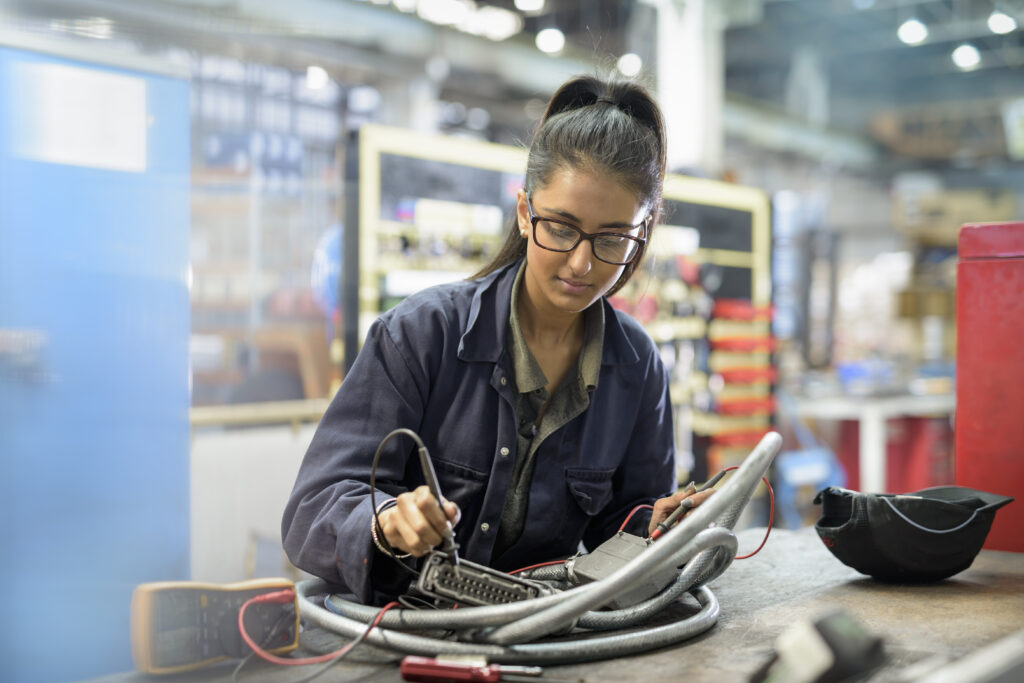 Female apprentice electricain uses a soldering iron in a car factory.