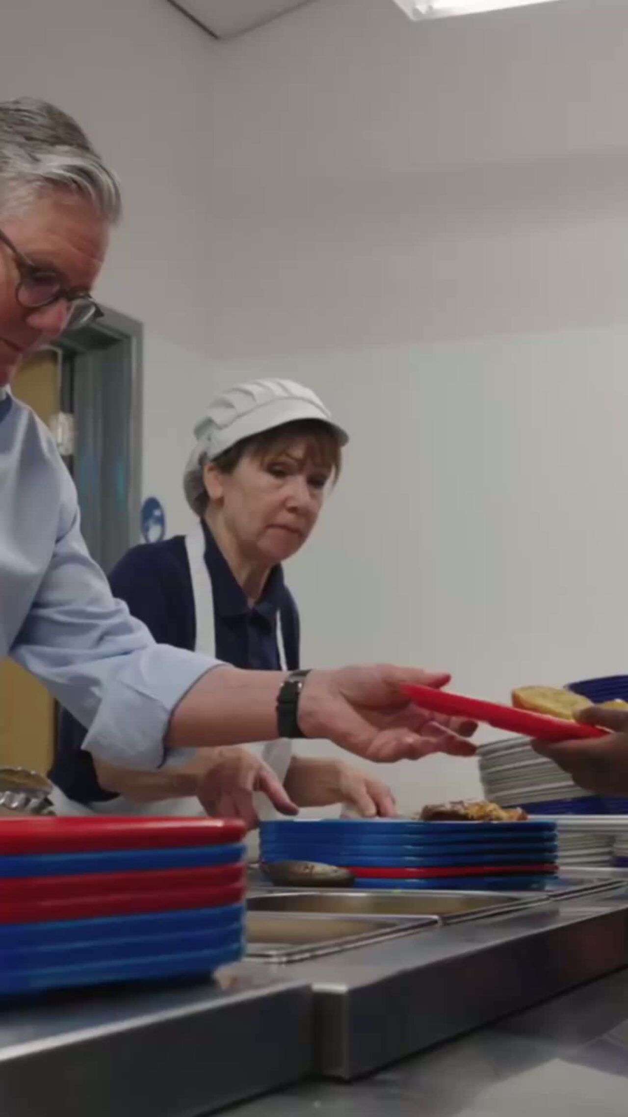 Prime Minister Keir Starmer serving food at a school canteen.