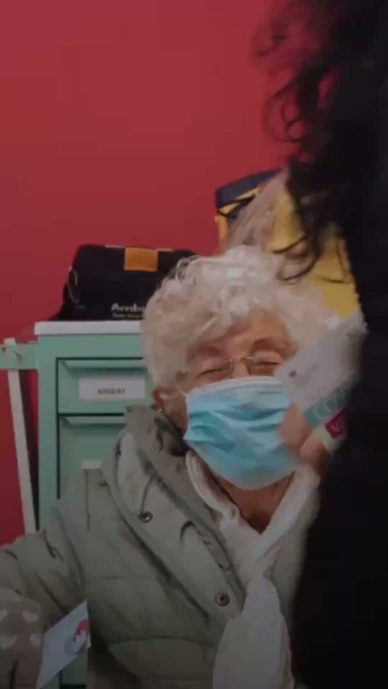 A woman wearing a facemask being looked after by a nurse.